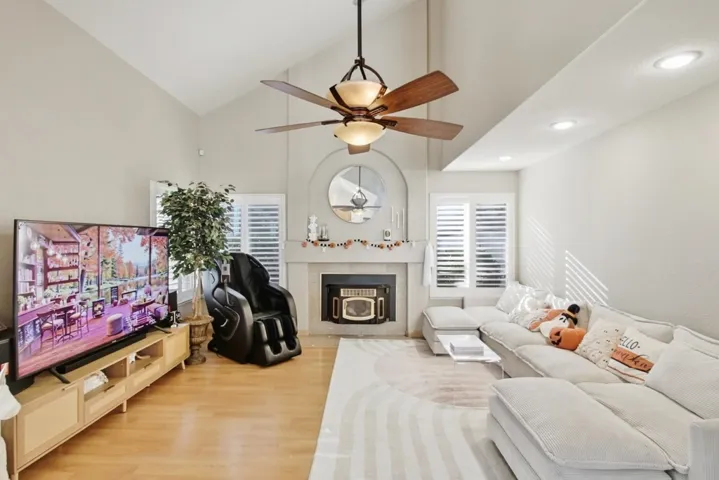 Living room with high vaulted ceiling, light wood-style floors, a fireplace with flush hearth, a ceiling fan, and recessed lighting