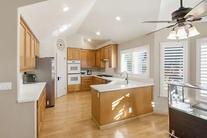 Kitchen with light countertops, a peninsula, ceiling fan, double oven, and light wood-style flooring