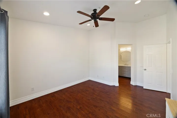 Primary bedroom with hardwood floors, ceiling fan, and recessed lights.