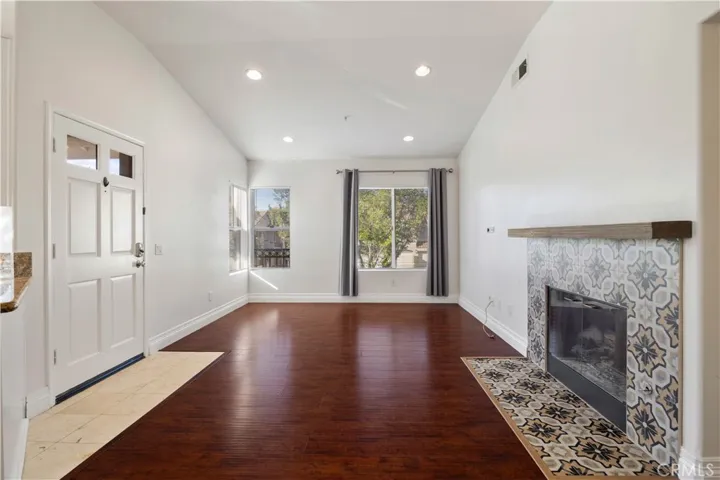 Living room has high ceilings, recessed lights, mosaic tiled fireplace and hardwood floors.