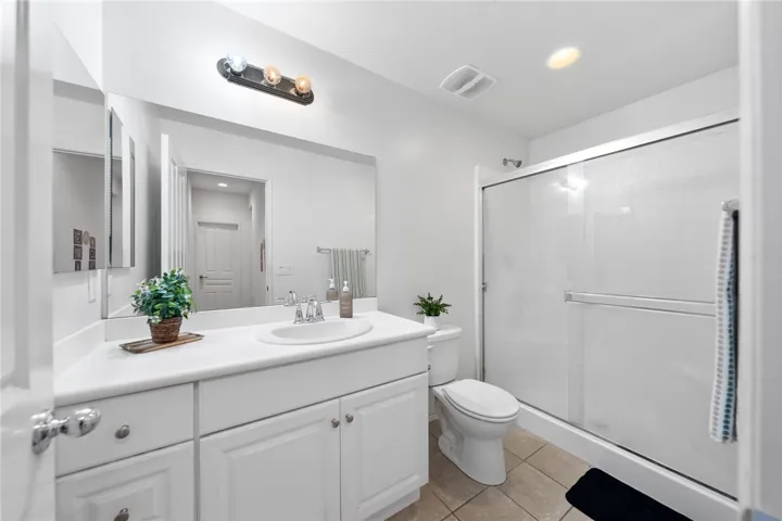 Clean, well-appointed bath with wide vanity, oversized mirror, and a glass-enclosed tub/shower combo.
