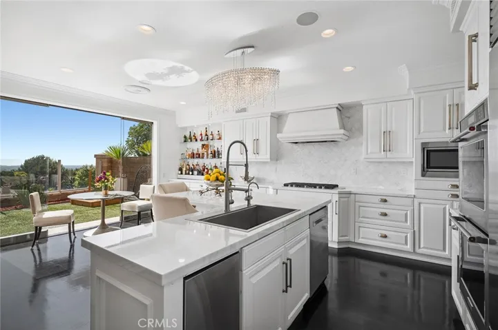  The chef-caliber kitchen is appointed with custom cabinetry, marble countertops, premium appliances, and a striking built-in bar. An oversized eat-in island anchors the space and flows seamlessly into the family room and expansive backyard.