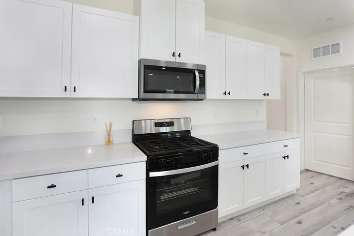 : Kitchen workspace featuring stainless steel gas range, built-in microwave, and full wall of cabinetry.