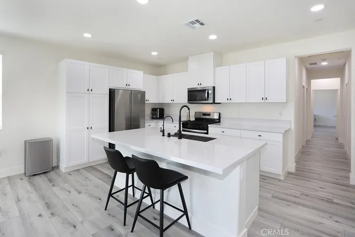 : Bright, modern kitchen featuring white cabinetry, quartz countertops, stainless steel appliances, and a large center island with seating.