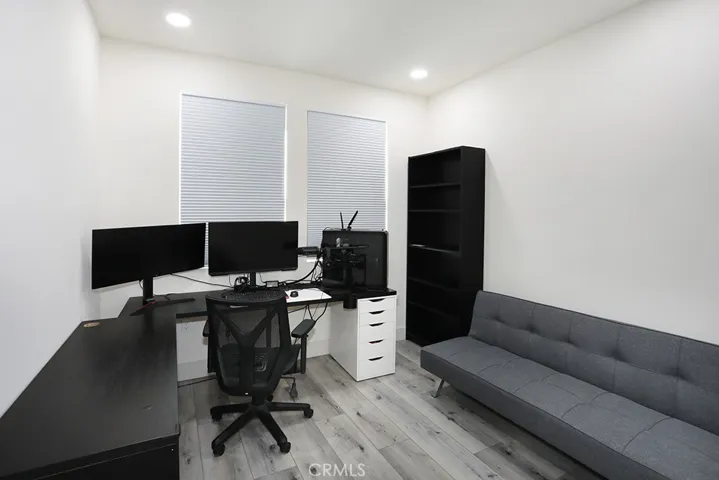 Bedroom currently used as a home office, featuring recessed lighting, neutral flooring, and multiple windows.
