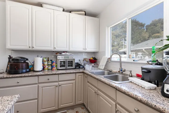 Kitchen with backsplash, light stone counters, and white cabinets