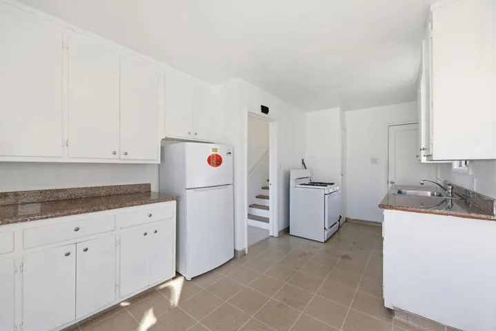 Kitchen featuring white appliances, white cabinets, and dark stone countertops