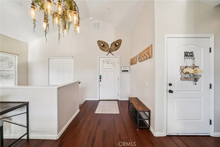 Vaulted entry with warm plank floors, statement chandelier, and handy hooks/bench leading into the main living level.