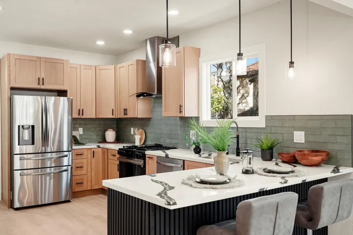 Kitchen with appliances with stainless steel finishes, a peninsula, hanging light fixtures, a kitchen bar, and light brown cabinets