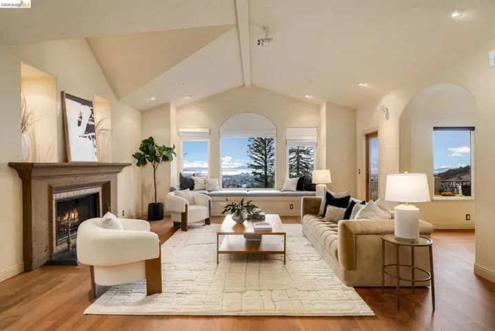 Living area with a warm lit fireplace, wood finished floors, recessed lighting, and high vaulted ceiling