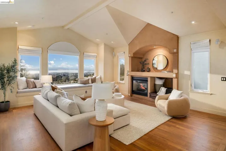 Living area featuring beam ceiling, wood finished floors, a glass covered fireplace, high vaulted ceiling, and recessed lighting