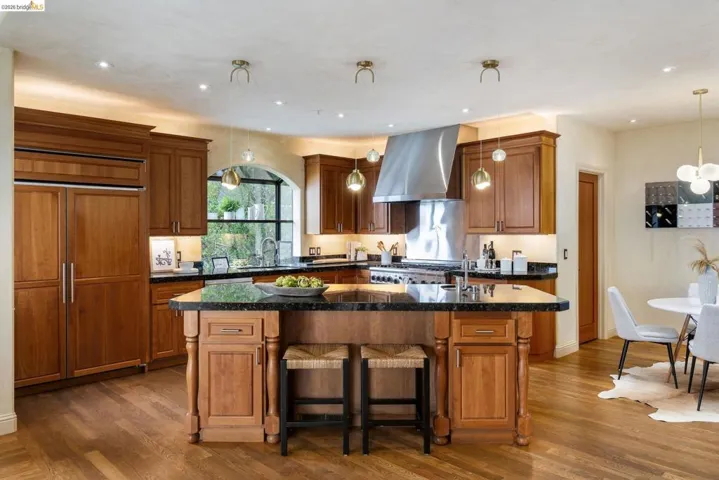 Kitchen with a center island with sink, brown cabinets, hanging light fixtures, a breakfast bar, and dark wood finished floors