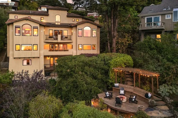 Back of property at dusk with stucco siding, a balcony, a wooden deck, a fire pit, and a chimney