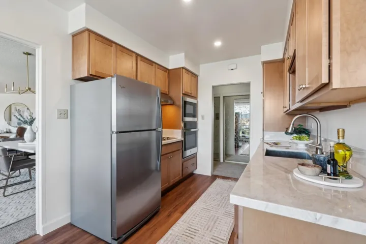 Kitchen featuring appliances with stainless steel finishes, light stone counters, dark wood-style flooring, under cabinet range hood, and brown cabinets