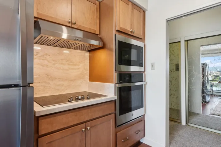 Kitchen with stainless steel appliances, under cabinet range hood, light stone counters, and brown cabinets