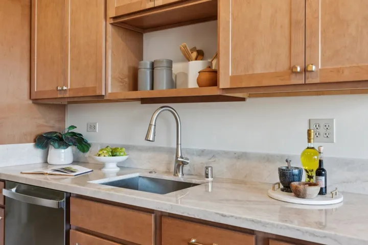 Kitchen featuring open shelves, dishwasher, and light stone countertops