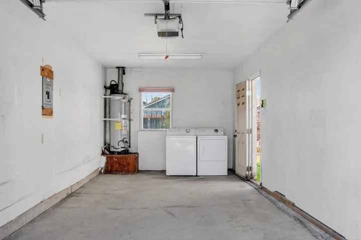 Garage with washing machine and dryer, gas water heater, a garage door opener, and electric panel