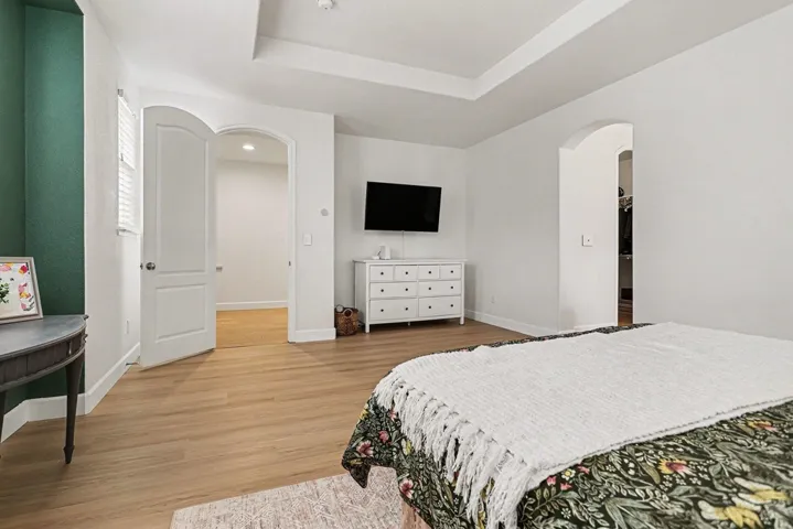 Bedroom with arched walkways, light wood-style floors, and a raised ceiling