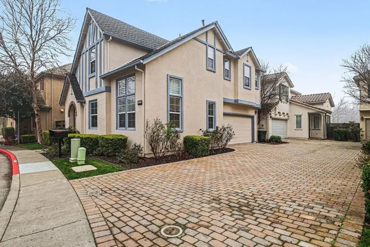View of side of property featuring stucco siding, decorative driveway, and an attached garage