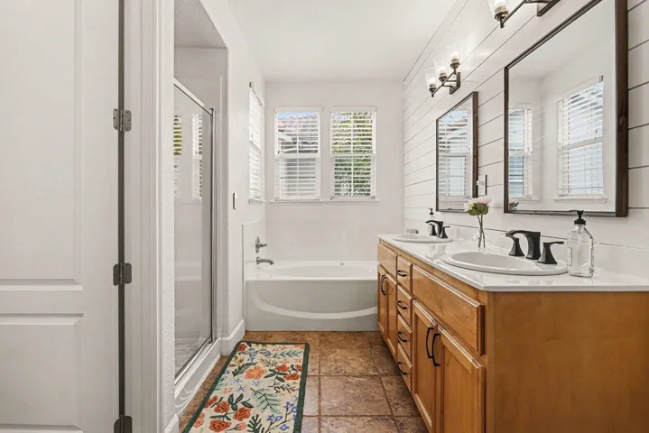 Full bathroom with a shower stall, double vanity, a bath, and stone tile floors