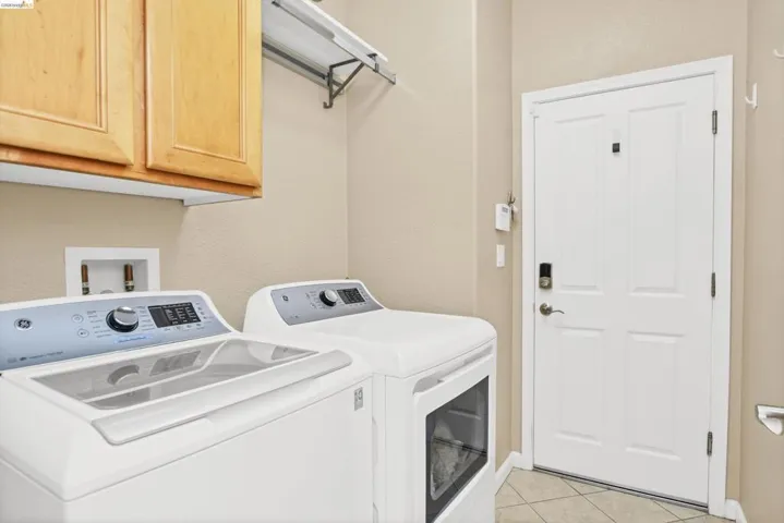 Washroom with cabinet space, light tile patterned flooring, washing machine and dryer, and a textured wall