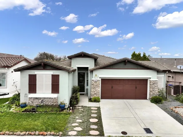 View of front of property with a tile roof, stone siding, stucco siding, a garage, and driveway