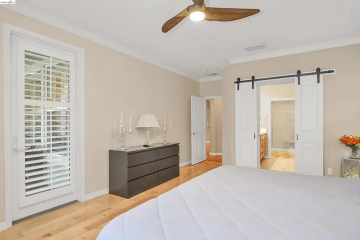 Bedroom featuring a barn door, light wood-style floors, crown molding, access to exterior, and ceiling fan