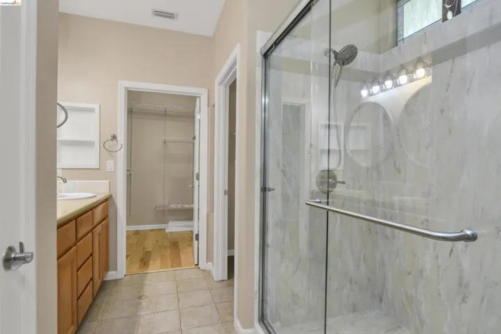 Full bath featuring vanity, a spacious closet, a marble finish shower, and light tile patterned flooring