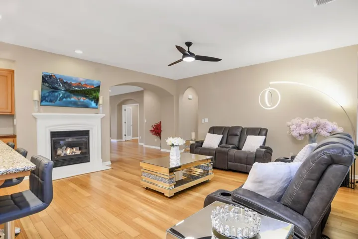 Living room with a glass covered fireplace, light wood-type flooring, ceiling fan, arched walkways, and recessed lighting