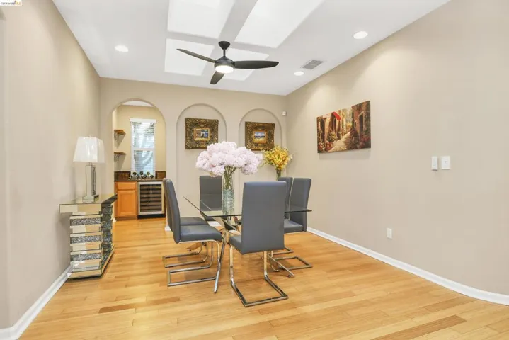 Dining space with a skylight, light wood-type flooring, beverage cooler, arched walkways, and a ceiling fan