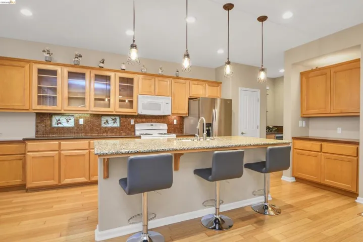 Kitchen featuring a kitchen breakfast bar, light wood-style floors, backsplash, white appliances, and glass insert cabinets