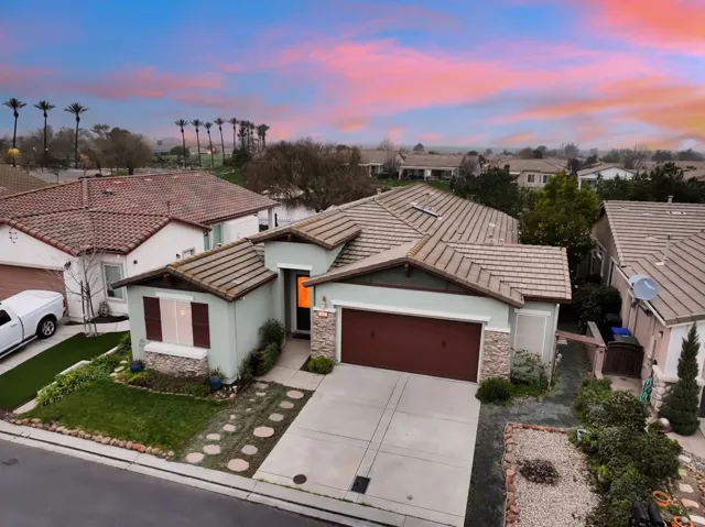View of front of property with an attached garage, stucco siding, stone siding, driveway, and a tile roof