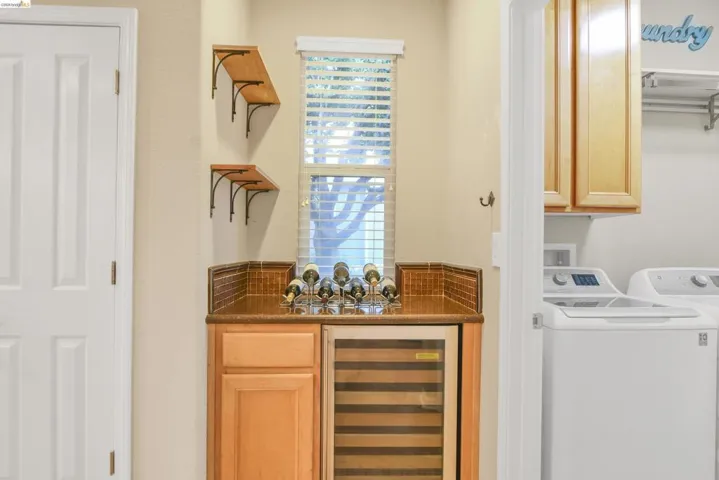 Indoor bar featuring beverage cooler, separate washer and dryer, light brown cabinetry, and dark stone counters