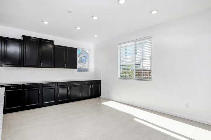 Kitchen with dark cabinetry, recessed lighting, light stone counters, and decorative backsplash