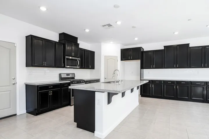 Kitchen with dark cabinetry, appliances with stainless steel finishes, decorative backsplash, light stone counters, and recessed lighting