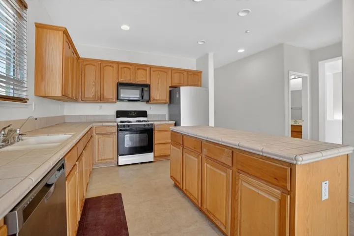 Kitchen featuring tile countertops, appliances with stainless steel finishes, a center island, and recessed lighting