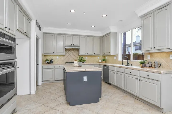 Kitchen with tile counters, appliances with stainless steel finishes, gray cabinetry, recessed lighting, and a center island