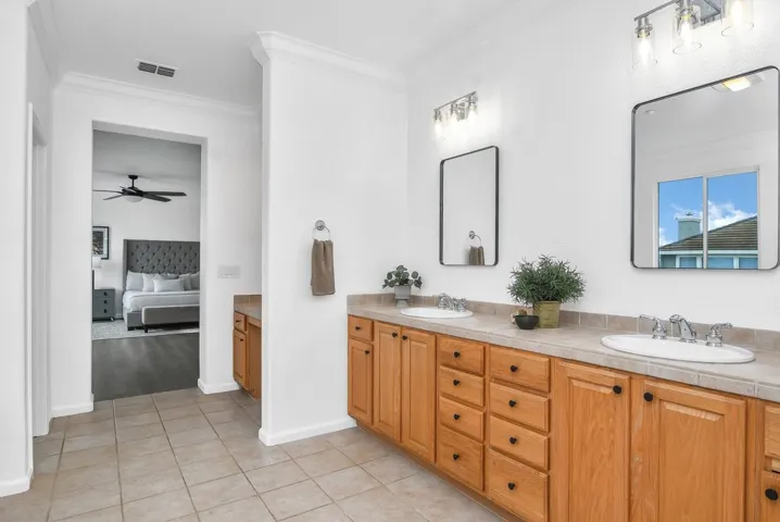 Full bath with ornamental molding, double vanity, connected bathroom, light tile patterned floors, and a ceiling fan