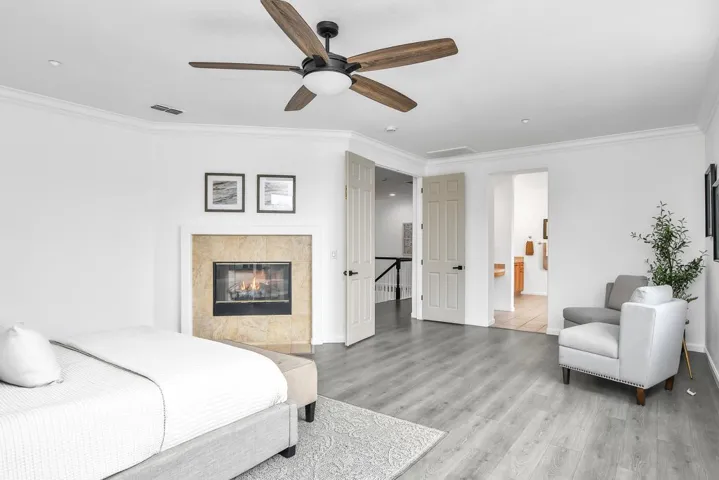 Bedroom with crown molding, ceiling fan, light wood-style floors, ensuite bathroom, and a tile fireplace