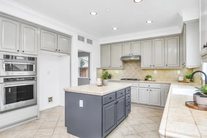 Kitchen with tile countertops, gray cabinets, double oven, a kitchen island, and crown molding
