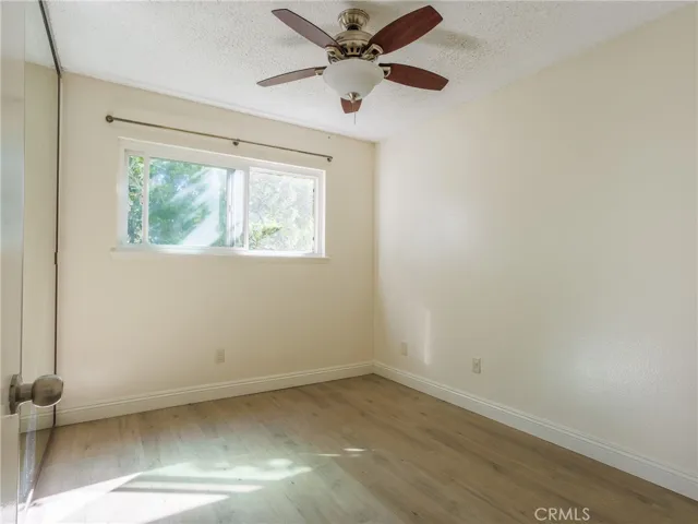 Bright bedroom or flex room featuring wood-style flooring, ceiling fan, and natural light from a large window.