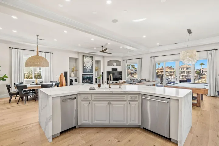 Kitchen featuring hanging light fixtures, light stone countertops, a center island with sink, ornamental molding, and recessed lighting