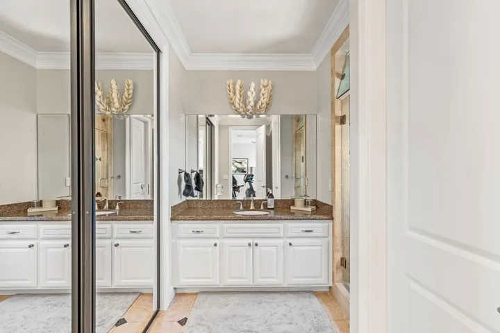 Bathroom featuring two vanities, crown molding, a shower stall, and light tile patterned flooring