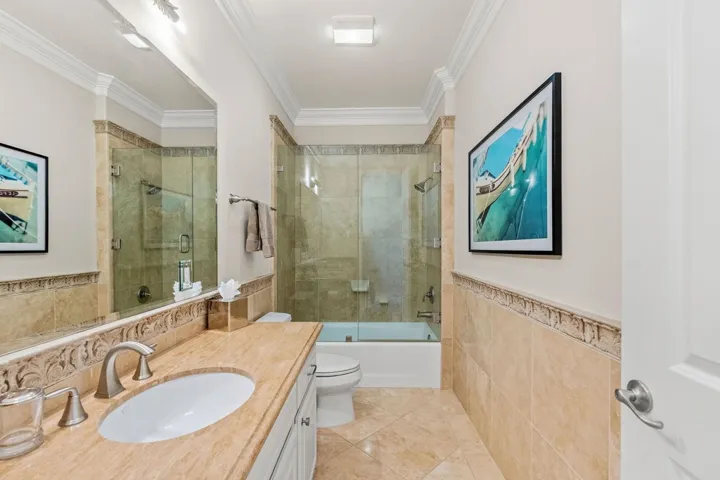 Full bathroom featuring tile walls, a wainscoted wall, vanity, combined bath / shower with glass door, and ornamental molding