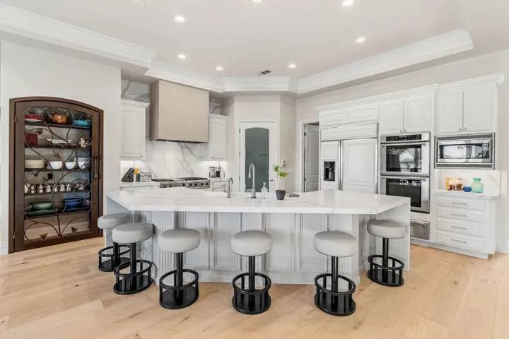 Kitchen featuring decorative backsplash, white cabinets, light wood-type flooring, a large island, and built in appliances