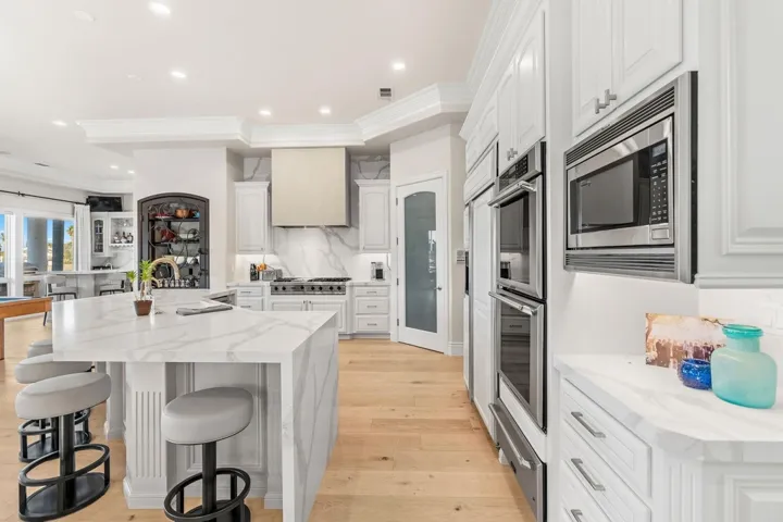 Kitchen featuring light stone countertops, white cabinets, light wood-style flooring, backsplash, and ornamental molding