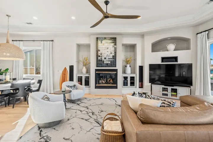 Living room featuring plenty of natural light, built in shelves, wood finished floors, ceiling fan, and ornamental molding