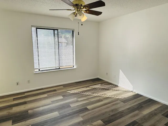 Empty room with a textured ceiling, dark wood-type flooring, and a ceiling fan
