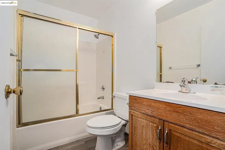 Full bath with bath / shower combo with glass door, vanity, and wood finished floors