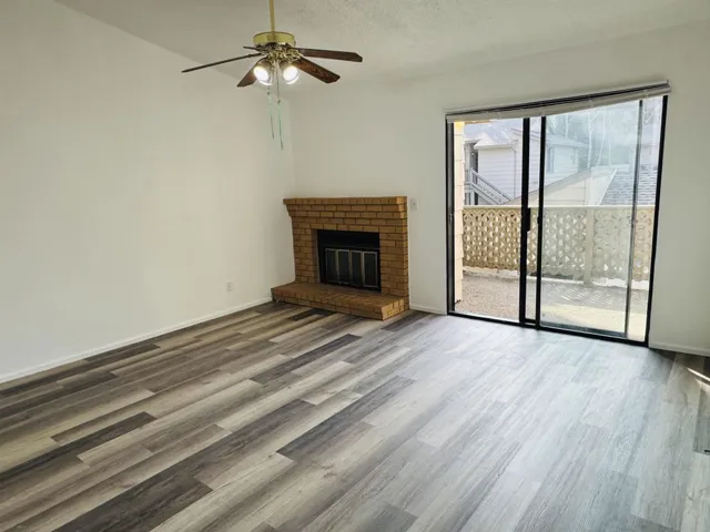 Unfurnished living room with a brick fireplace, wood finished floors, a ceiling fan, and a textured ceiling